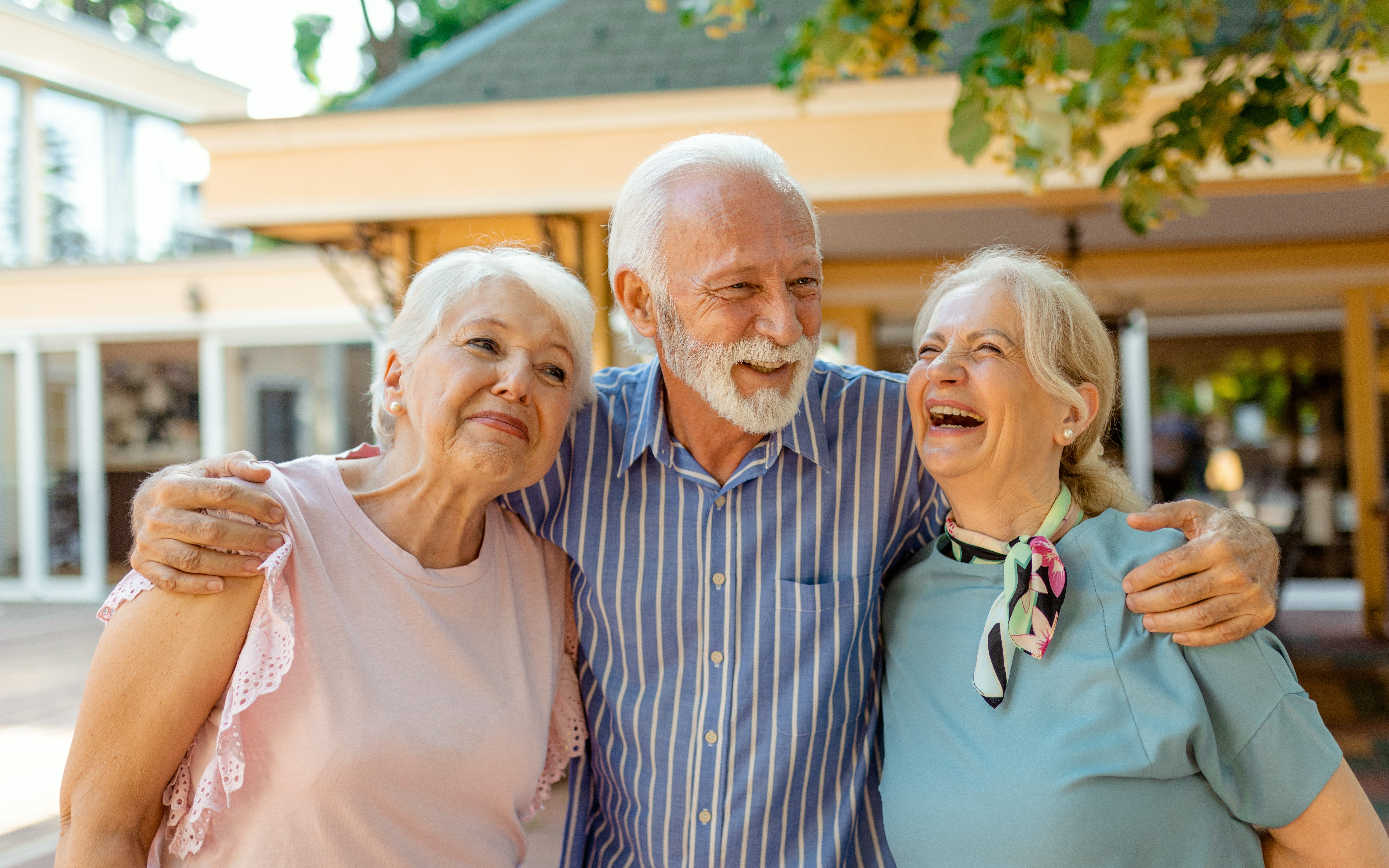 Three older adults smiling together outside a senior living community.